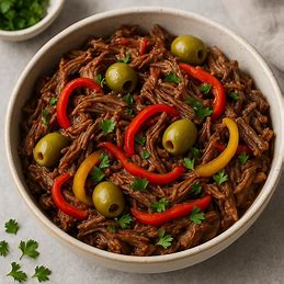 Carne desfiada em uma tigela com pimentões coloridos e azeitonas, guarnecida com salsa fresca.