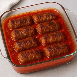 Bifes à rolê de carne em uma tigela de vidro, cozidos no forno em molho de tomate e prontos para servir.