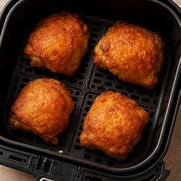 Coxas de frango crocantes em uma cesta de airfryer, com a pele dourada e apetitosa.