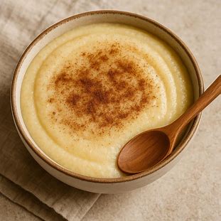 Tigela de mingau de fubá cremoso com canela polvilhada e colher de madeira.