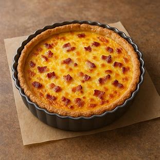 A imagem mostra uma torta salgada com massa crocante (massa quebrada) em uma forma de fundo removível, recheada com um creme dourado e pedacinhos de bacon visíveis na superfície.