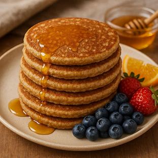 Imagem de panquecas integrais douradas empilhadas com mel e frutas ao lado, representando uma refeição saudável e nutritiva para café da manhã.
