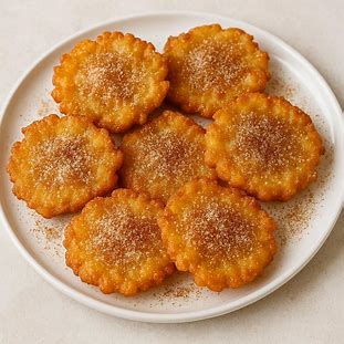 Bolinhos de chuva dourados polvilhados com açúcar e canela sobre prato branco.