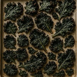 Chips de Couve Assada. Foto de folhas de couve escuras, com textura crocante, espalhadas em uma assadeira.