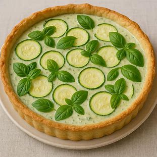 Quiche de Abobrinha e Manjericão. Foto de uma quiche fresca e clara, com massa quebrada nas laterais. O recheio cremoso e verde contém fatias finas de abobrinha e folhas de manjericão.