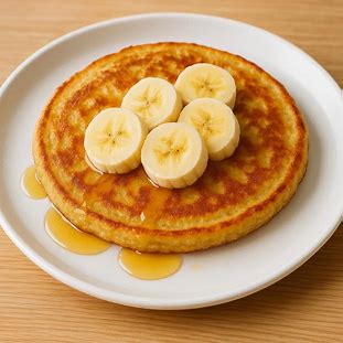 Panqueca de banana dourada, servida em prato branco com fatias de banana e mel, representando um café da manhã saudável e energético.