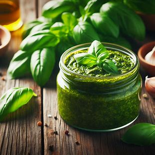 Molho pesto verde servido em pote de vidro com folhas de manjericão frescas ao redor.