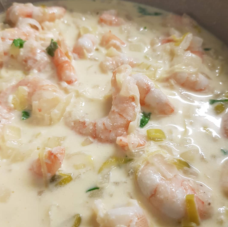 Camarões ao creme de alho-poró servidos em prato fundo, decorados com salsinha fresca.